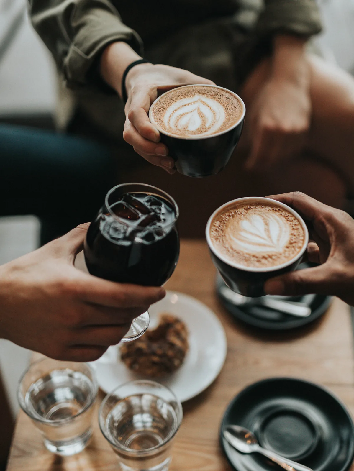 Varias manos brindando con tazas de caf&eacute; sobre una mesa de madera.