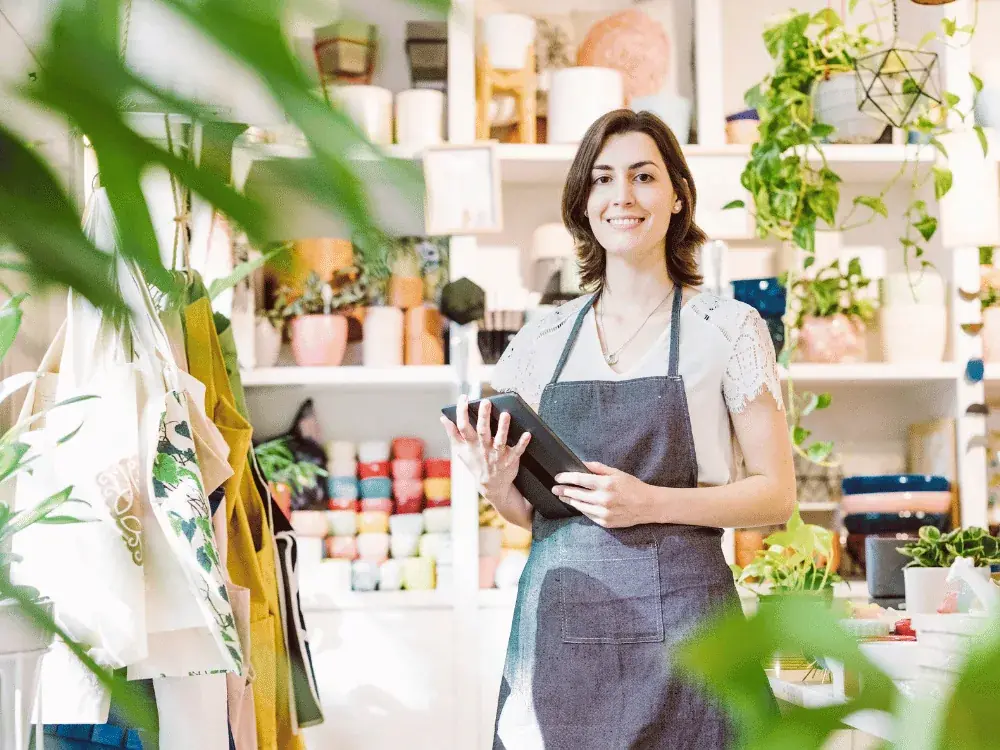 Due&ntilde;a de una tienda de plantas y objetos revisando una tablet entre sus estantes.